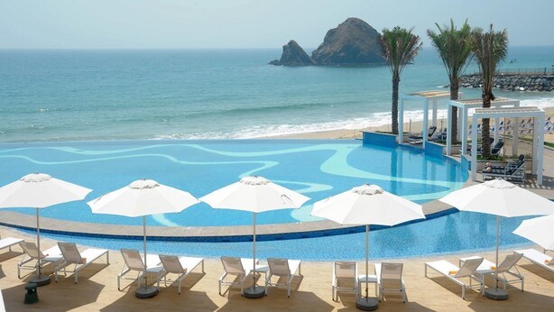 A pool with lounge chairs and umbrellas, overlooking the ocean and a rocky island. - Royal M Resort Al Aqah Beach Resort (Al Aqah)