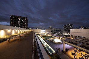 Terraza en la azotea con piscina, zonas de estar y vistas nocturnas de la ciudad.