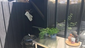 A small outdoor kitchen area with a grill, a table with potted plants, and a window with a view of the outside. - Holiday home, swimmingpool and beach (Nykøbing Sj)