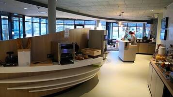 En moderne, veloplyst reception med en buet disk, kaffemaskine og et siddeområde med udsigt gennem store vinduer.