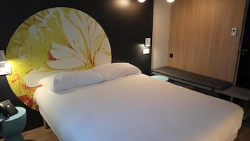 Quarto de hotel com uma cama grande, um ornamento circular na parede, uma mesa de cabeceira com luminária e um guarda-roupa de madeira.