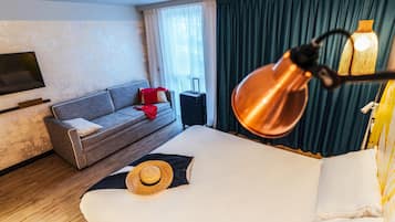 A hotel room with a bed, a sofa, a TV, a suitcase, and a lamp.