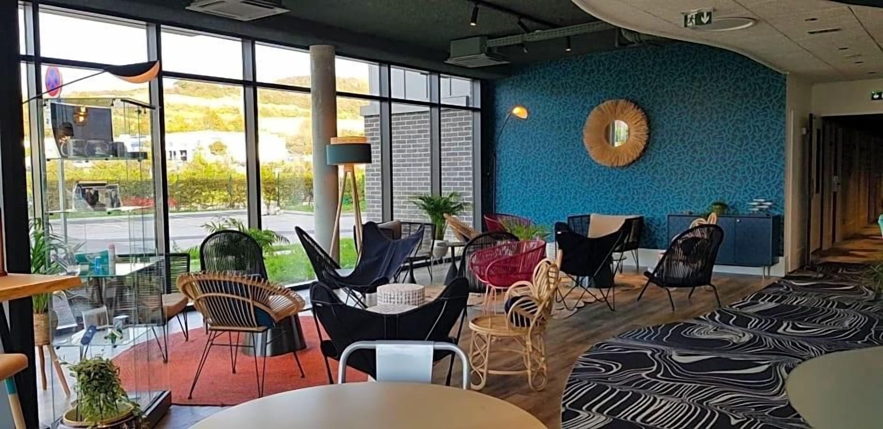 Un intérieur moderne avec de grandes fenêtres, un mur bleu à la texture intéressante et différents types d’espaces aménagés pour s’asseoir.