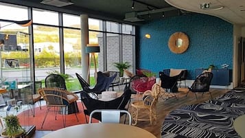 Un intérieur moderne avec de grandes fenêtres, un mur bleu à la texture intéressante et différents types d’espaces aménagés pour s’asseoir.