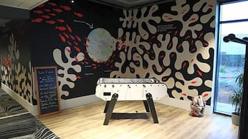 Une pièce avec un baby-foot, une grande fresque murale abstraite et une fenêtre donnant sur un beau paysage.