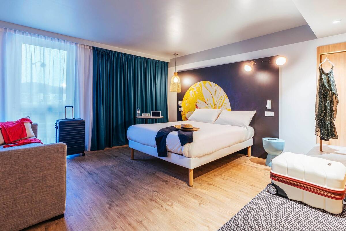 Ein modernes Hotelzimmer mit einem Bett, einem Schreibtisch, einem Stuhl, einem Koffer und einem Kleiderschrank.