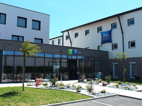 A modern building with a glass facade, outdoor seating, and a garden area. - Ibis Styles Le Treport Mers Les Bains (Mers-les-Bains)