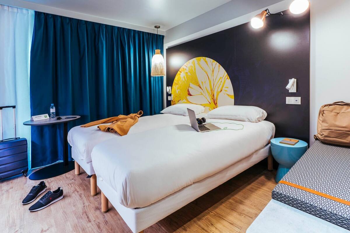 Ein Hotelzimmer mit Bett, Schreibtisch, Stuhl, Koffer und einem Fenster mit Vorhängen.