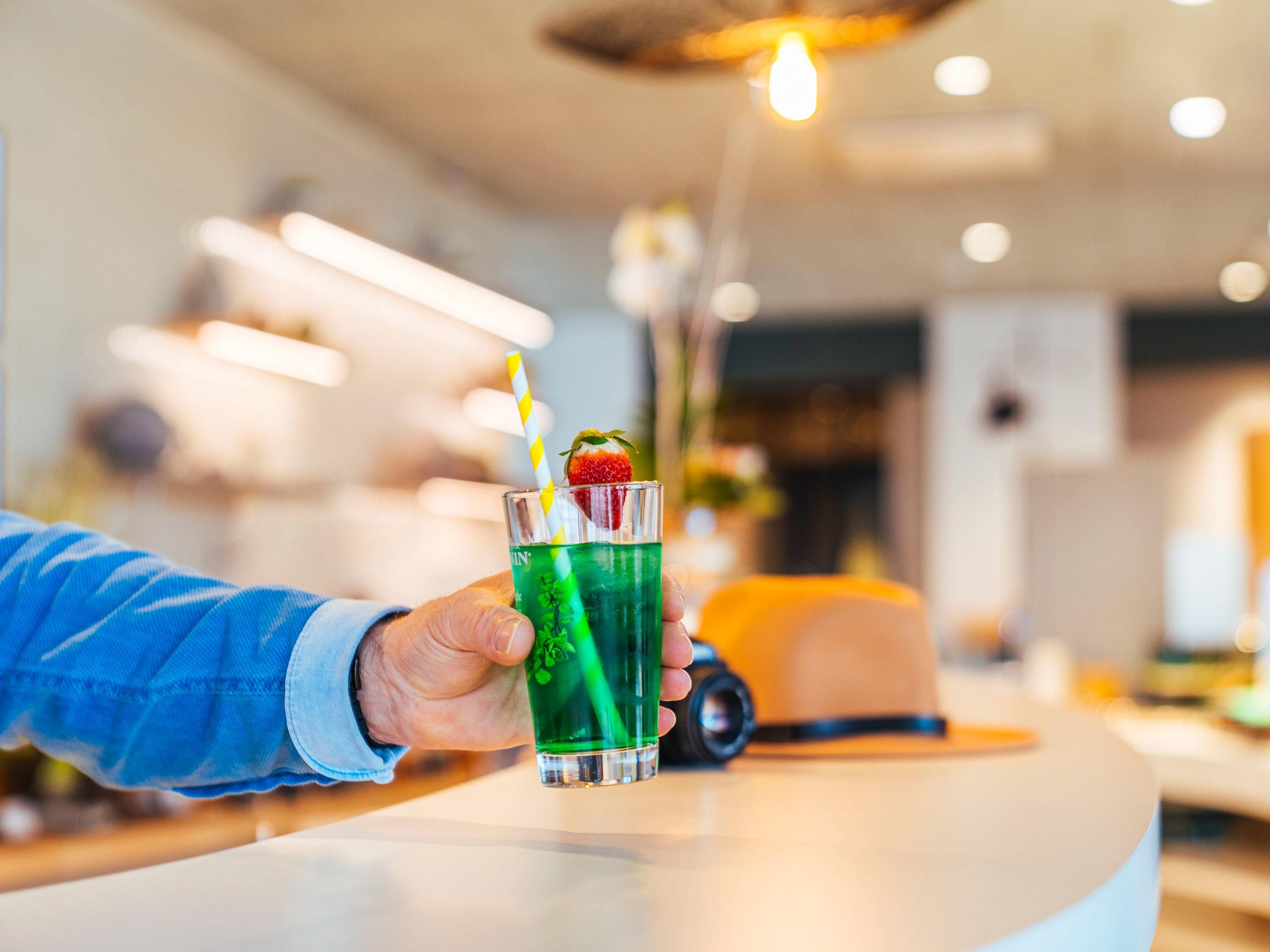 Una mano sosteniendo un vaso con una bebida verde, una pajita y una fresa como adorno.