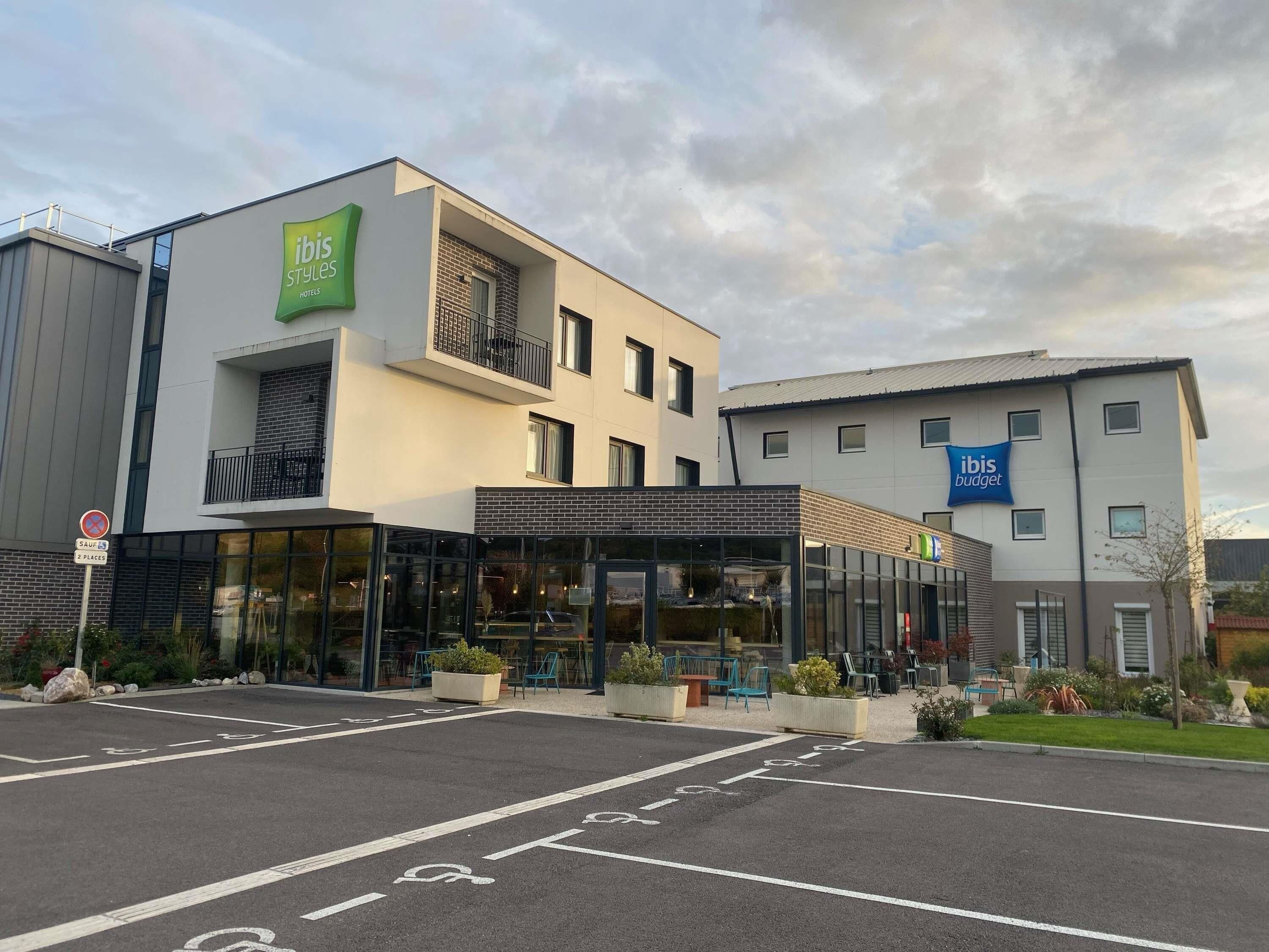 A modern hotel with a glass facade, a balcony, and a sign for 'ibis Styles Hotels'.