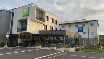 A modern hotel with a glass facade, a balcony, and a sign for 'ibis Styles Hotels'.
