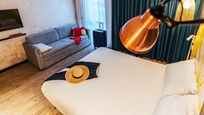 A hotel room with a bed, a sofa, a TV, a suitcase, and a lamp. - Ibis Styles Le Treport Mers Les Bains (Mers-les-Bains)