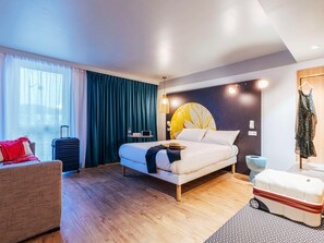 A modern hotel room with a bed, a desk, a chair, a suitcase, and a wardrobe. - Ibis Styles Le Treport Mers Les Bains (Mers-les-Bains)