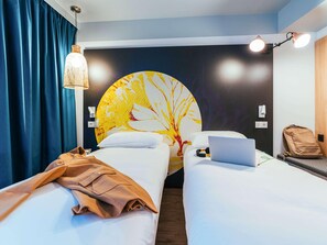 A hotel room with two beds, a laptop on one bed, a backpack on the other, and a large circular wall decoration. - Ibis Styles Le Treport Mers Les Bains (Mers-les-Bains)
