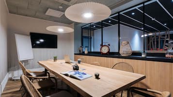 A conference room with a long table, chairs, a whiteboard, a clock, and a window with a view.