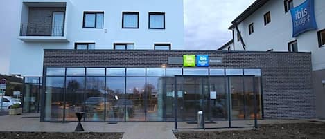 Un bâtiment moderne avec une entrée en verre, une façade en briques et une enseigne indiquant « ibis budget ».