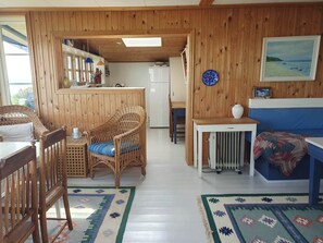 L’intérieur chaleureux d’un chalet comprend un coin repas, un fauteuil en osier, un canapé bleu et un espace cuisine.