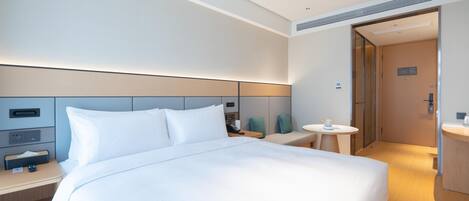 A modern hotel room with a large bed, bedside tables, a small round table, and a separate bathroom area.