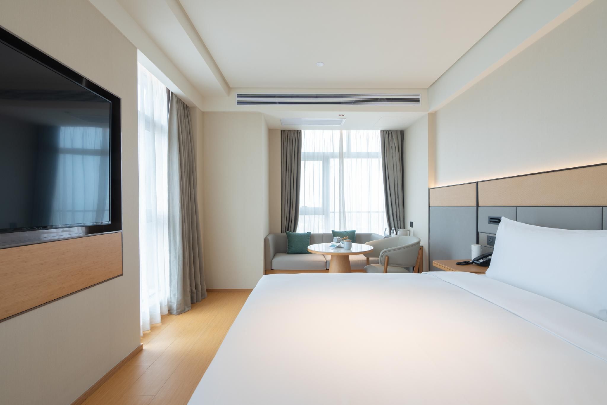 Een hotelkamer met een groot bed, een televisie, een bank, een kleine ronde tafel en een stoel.