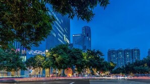 A cityscape at dusk with modern high-rise buildings, a crosswalk, and trees lining the street. - Guangzhou Tianhe Sports Center Mercure Hotel (Guangzhou)
