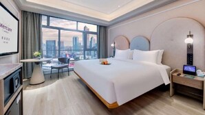 A hotel room with a bed, a desk, a chair, a small table, and a view of the cityscape. - Guangzhou Tianhe Sports Center Mercure Hotel (Guangzhou)