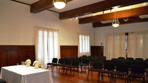 A conference room with a white table, black chairs, wooden beams, and large windows with curtains. - DM Hoteles Mossone Ica (Ica)