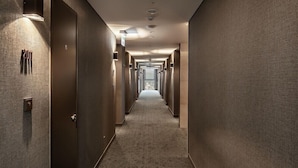 Un long couloir étroit, avec des portes de chaque côté, un sol recouvert de moquette et des spots encastrés au plafond.