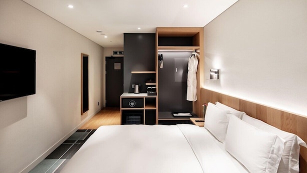 Une chambre d’hôtel moderne dotée d’un grand lit, d’un téléviseur fixé au mur, d’un dressing et d’une petite kitchenette.