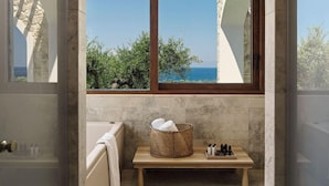 Ein Badezimmer mit einer Badewanne, einer Holzbank, einem Korbwannen und Meerblick.