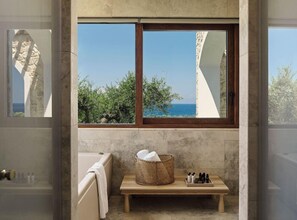 A bathroom with a bathtub, a wooden bench, a wicker basket, and a view of the sea. - Lesante Cape Resort & Villas (Zakynthos)