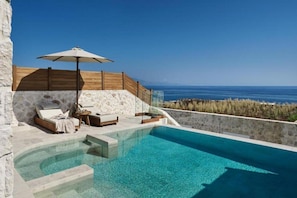 A poolside area with a clear view of the sea, a wooden deck, and a stone wall. - Lesante Cape Resort & Villas (Zakynthos)