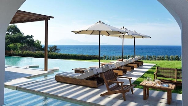 Ein Poolbereich mit Liegestühlen, Sonnenschirmen und Blick auf das Meer.