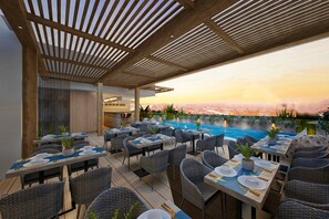 An outdoor dining area with tables and chairs, a pool, and a view of the cityscape at sunset. - Bayfront Hotel Cebu Capitol Site (Cebu City)