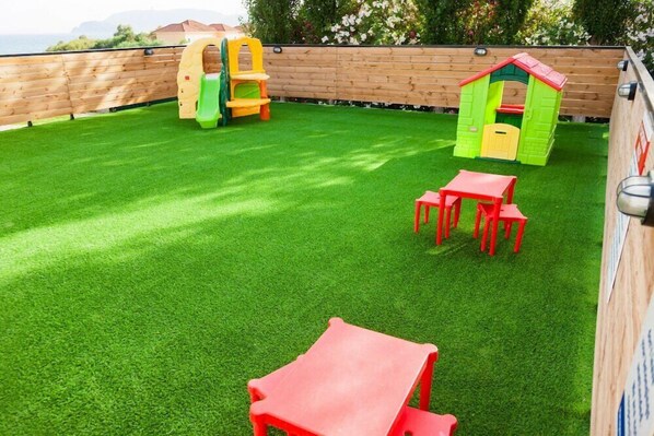 A backyard with artificial grass, a playhouse, and a small table and chairs. - Cavo Suites - Adults Only (Zakynthos)