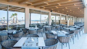 Een terras met tafels en stoelen, grote ramen en uitzicht op het strand.