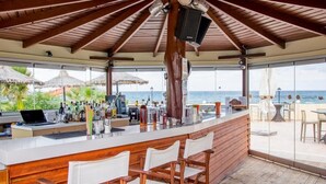 Een bar met houten plafond, barstoelen, een laptop en uitzicht op de oceaan.