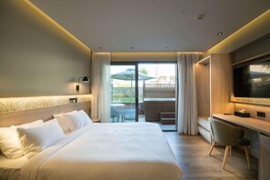 Ein Hotelzimmer mit einem großen Bett, einem Schreibtisch, einem Fernseher und einem Balkon mit Tisch und Stühlen.