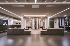 Un vestíbulo moderno con una zona de estar central, un mostrador de recepción y una escalera que conduce a pisos superiores.