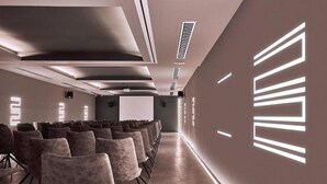 A conference room with rows of chairs facing a projection screen, a long table, and a modern ceiling design. - Nema Design Hotel and Spa - Adults Only (Hersonissos)