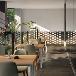 A modern dining area with tables and chairs, a glass partition, and potted plants. - Hotel 88 Blok M (Jakarta)