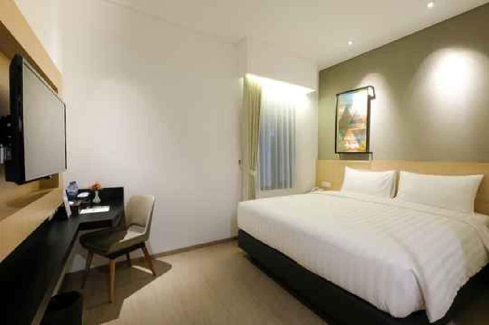 A hotel room with a bed, a desk, a chair, a TV, and a window with curtains.