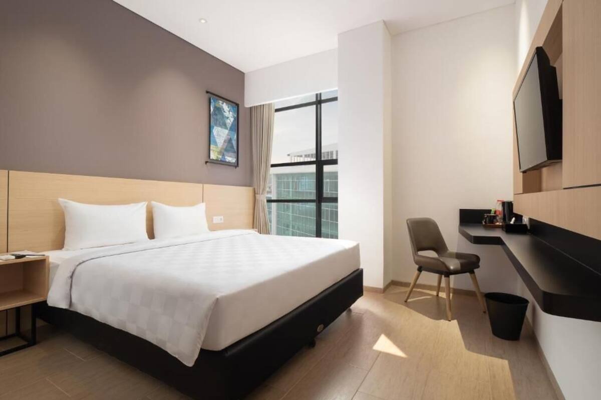 A hotel room with a bed, a desk, a chair, a TV, and a window.