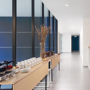 A long table with multiple white cups and saucers, a coffee machine, and a vase with dried plants. - Hotel 88 Blok M (Jakarta)