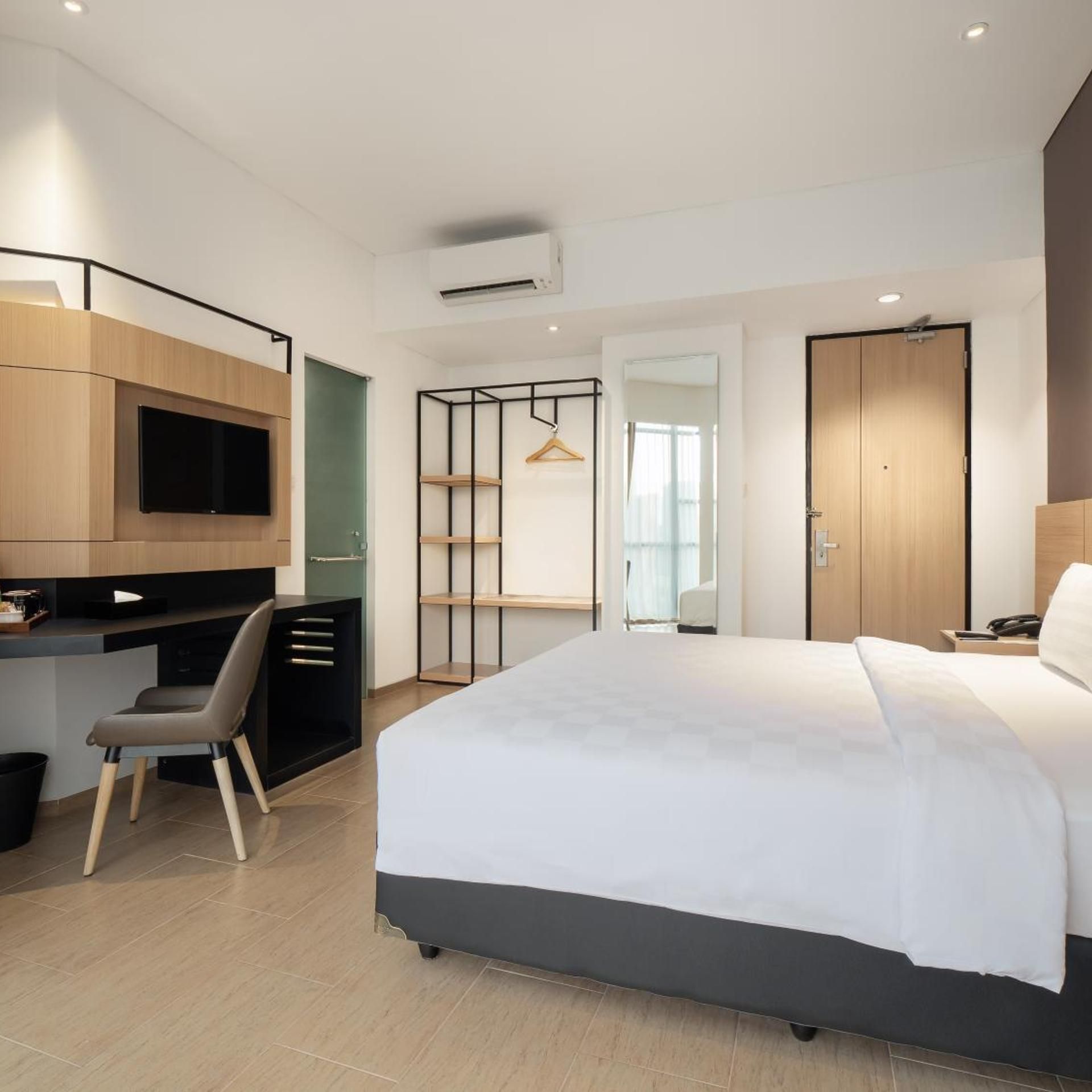A modern hotel room with a bed, a desk, a chair, a TV, a wardrobe, and a mirror.