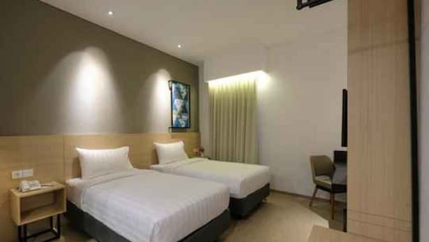A hotel room with two beds, a desk, a chair, and a painting on the wall. - Hotel 88 Blok M (Jakarta)