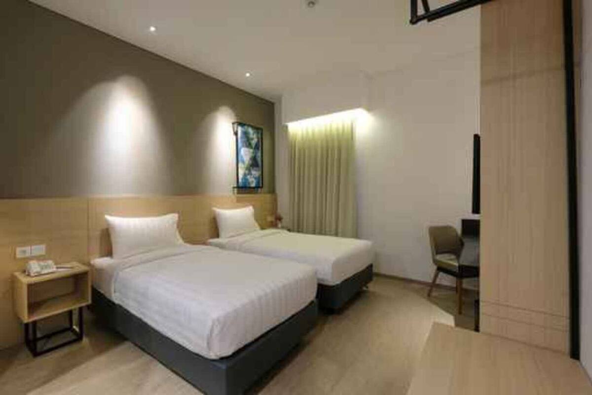 A hotel room with two beds, a desk, a chair, and a painting on the wall.