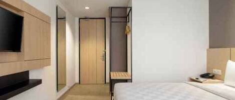 A hotel room with a bed, a TV mounted on the wall, a wardrobe, and a door leading to another room.