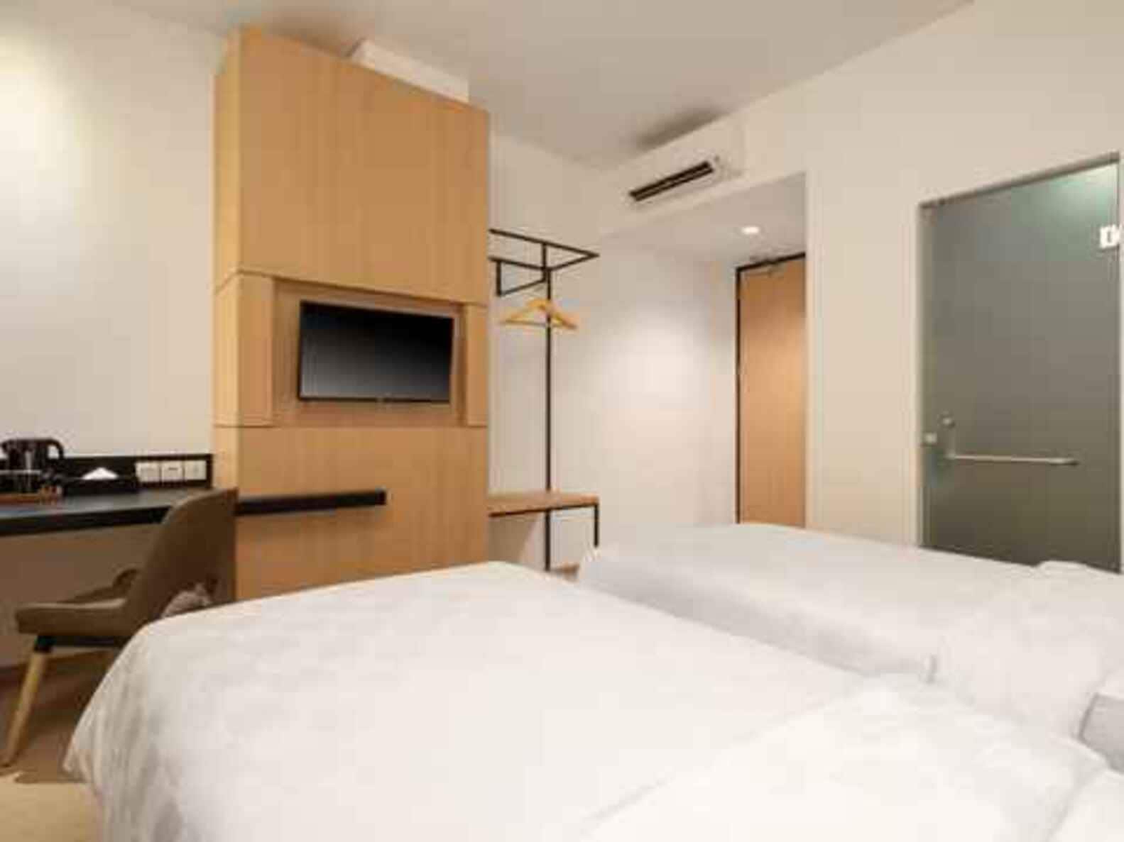A hotel room with two beds, a desk with a flat-screen TV, a chair, and a wardrobe.