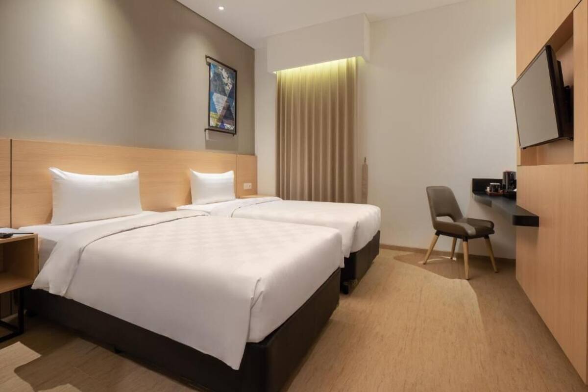 A hotel room with two beds, a desk, a chair, a TV, and a curtain.