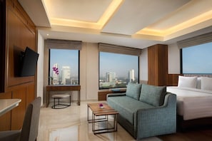 A hotel room with a bed, sofa, TV, and a city view. - Trembesi Hotel BSD (South Tangerang)